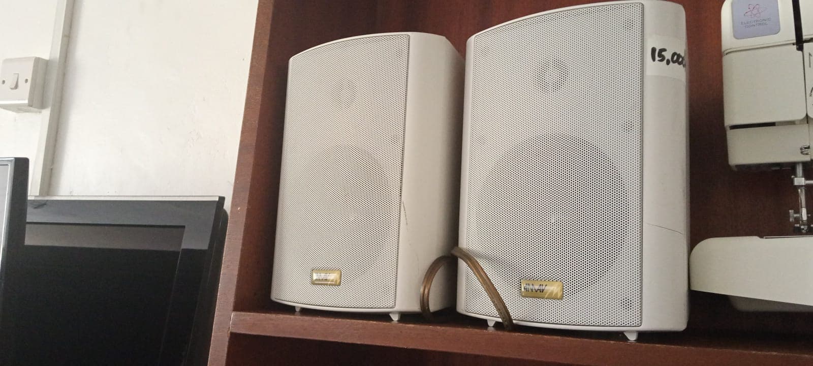 Two white speakers with mesh grilles on a wooden shelf, one with a price tag.