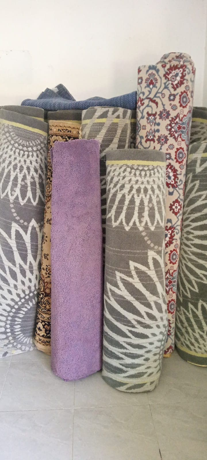 Rolled rugs with grey floral and purple patterns leaning against a white wall on tiles.