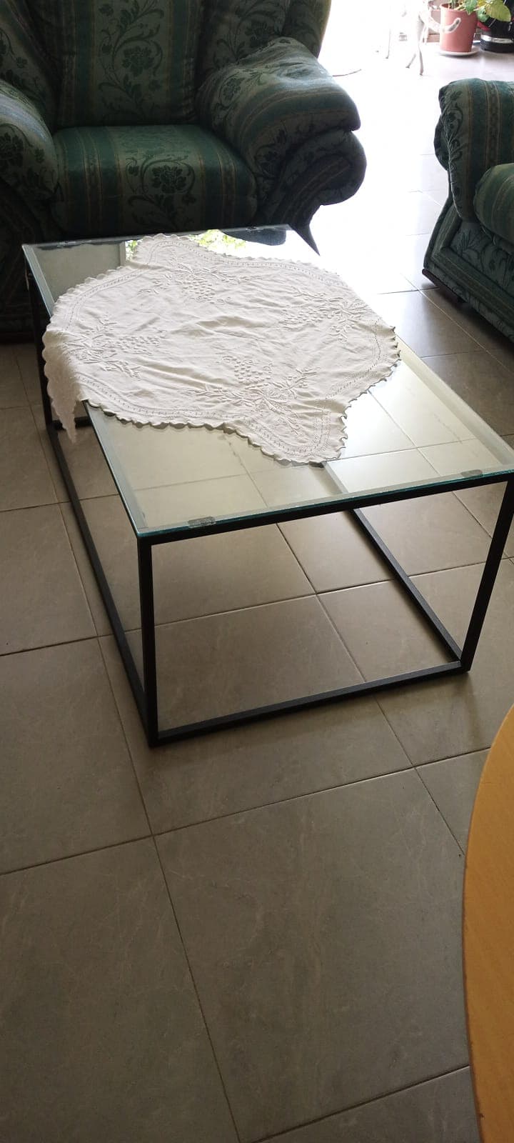 Rectangular glass coffee table with a black metal frame and a white lace doily.