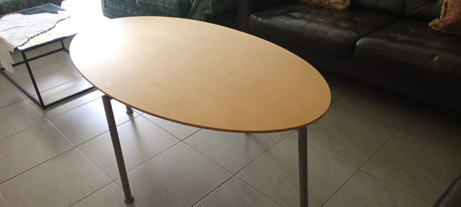 Oval light wood table with thin grey metal legs on a grey tiled floor.